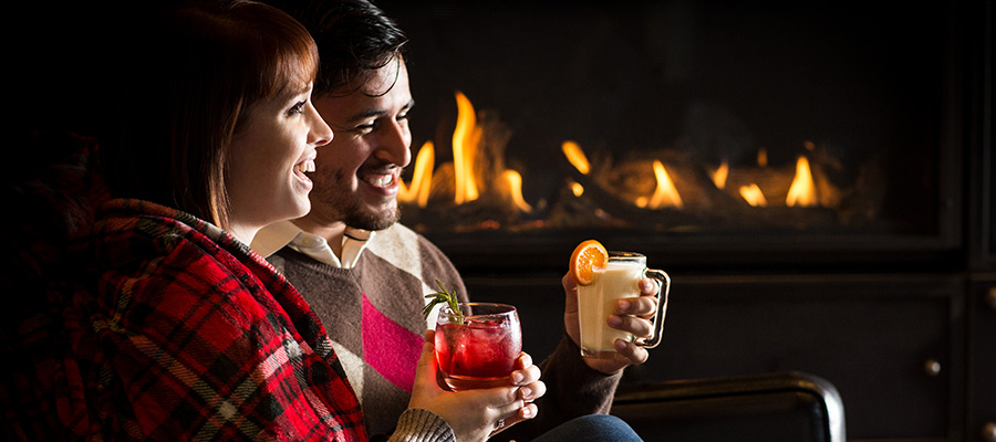 couple sitting by fire with specialty winter drinks